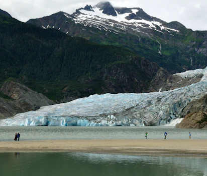 Turister udforsker Mendenhall Gletsjer strand i Juneau Alaska med sne-dækkede bjerge