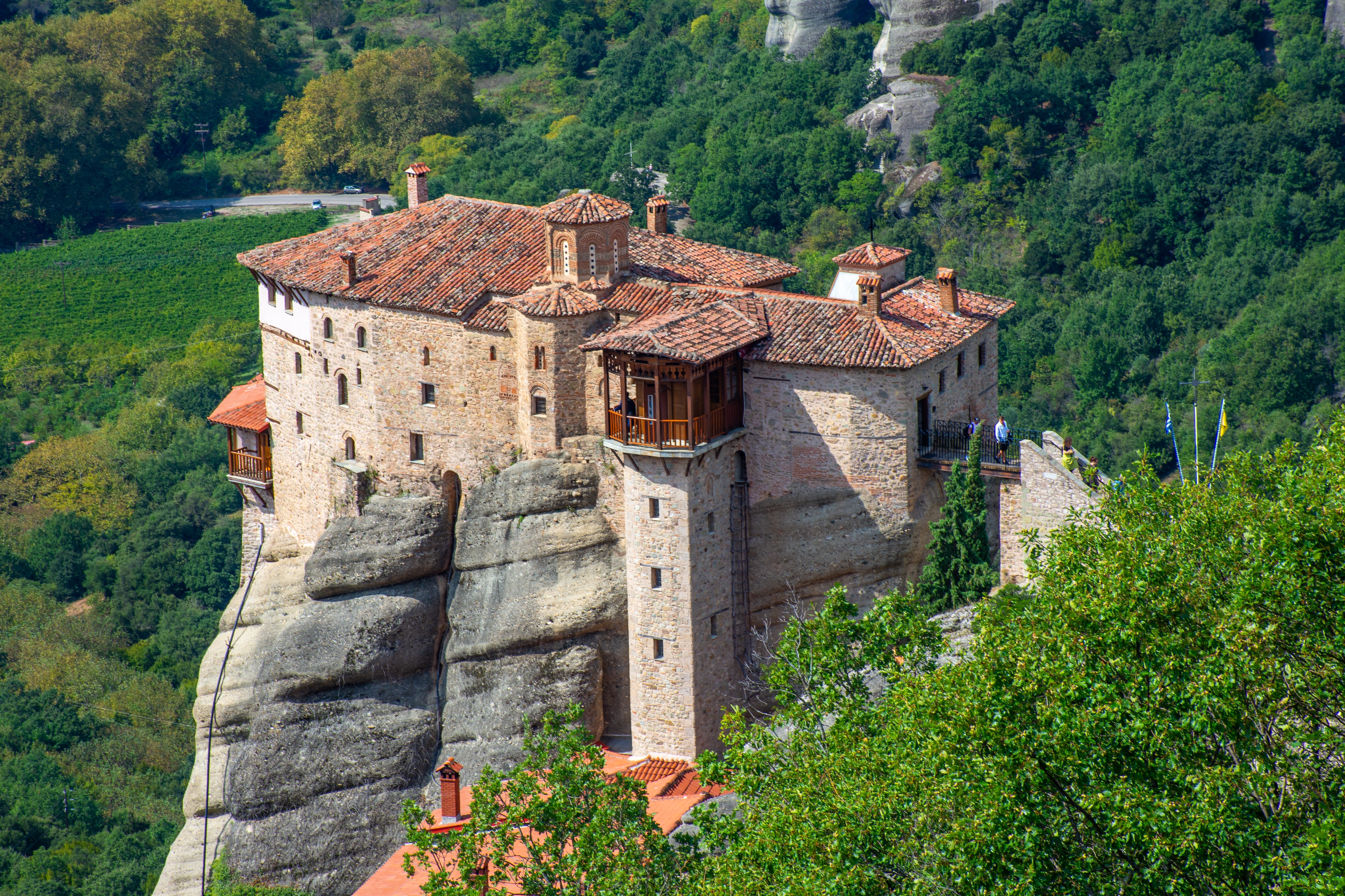 Meteora kloster på dramatiske klippetop i Grækenland med traditionelt rødt tegltag omgivet af frodig skov
