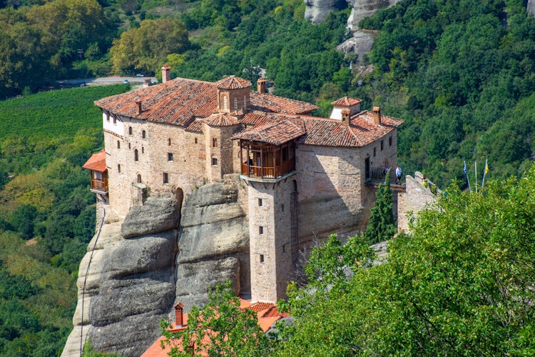 Meteora kloster på dramatiske klippetop i Grækenland med traditionelt rødt tegltag omgivet af frodig skov