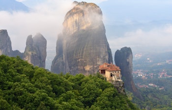 Det hellige Roussanou kloster bygget på toppen af en dramatisk klippe i Meteora, omgivet af morgentåge ved solopgang i Kastraki, Grækenland