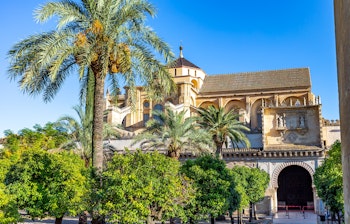 Den historiske Mezquita-katedral i Córdoba med maurisk arkitektur, palmtræer og den smukke orangehave under en klar blå himmel i Andalusien, Spanien