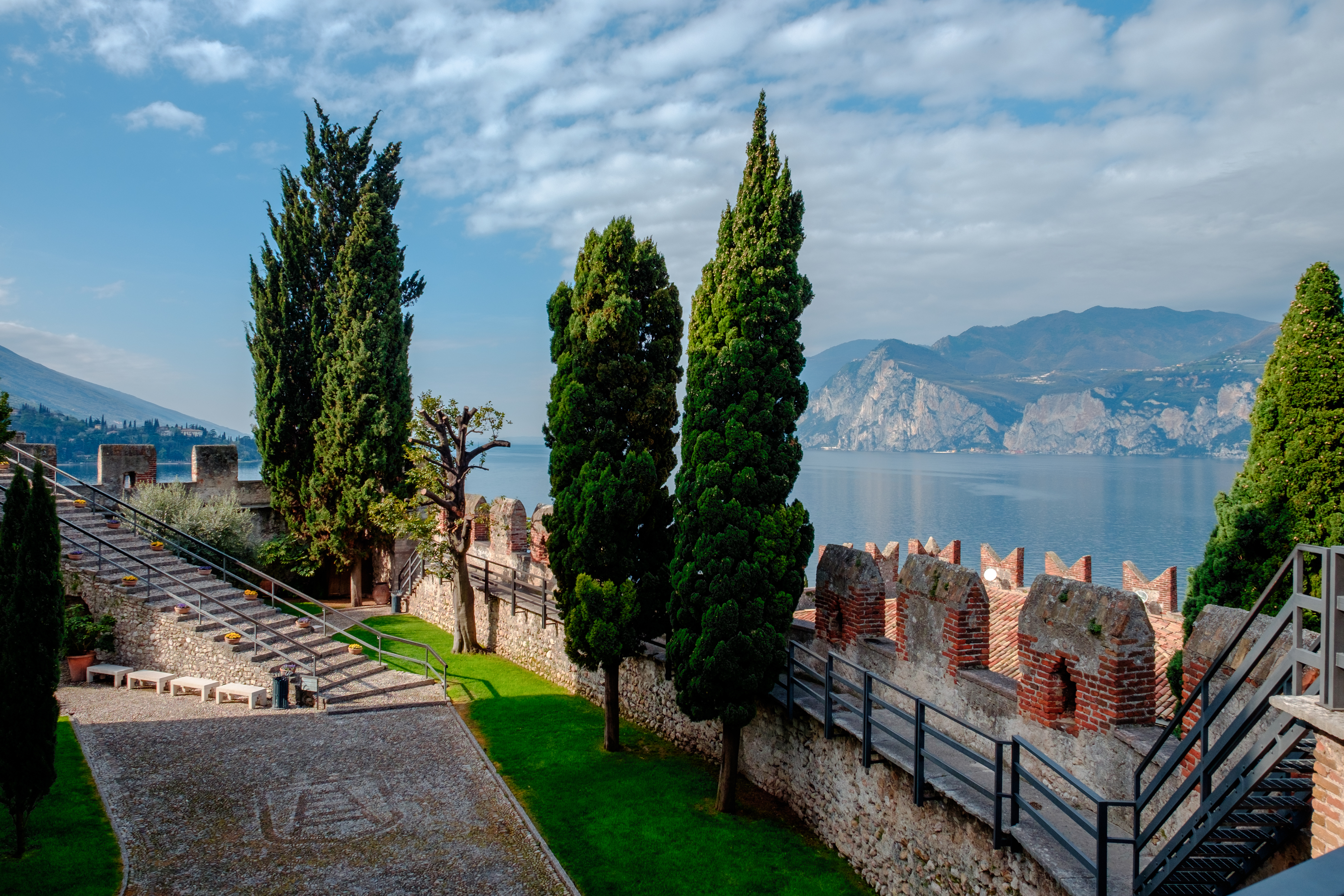 Historisk middelalderborg med tårnmure ved Gardasøen i Italien omgivet af høje cypresser og bjerglandskab