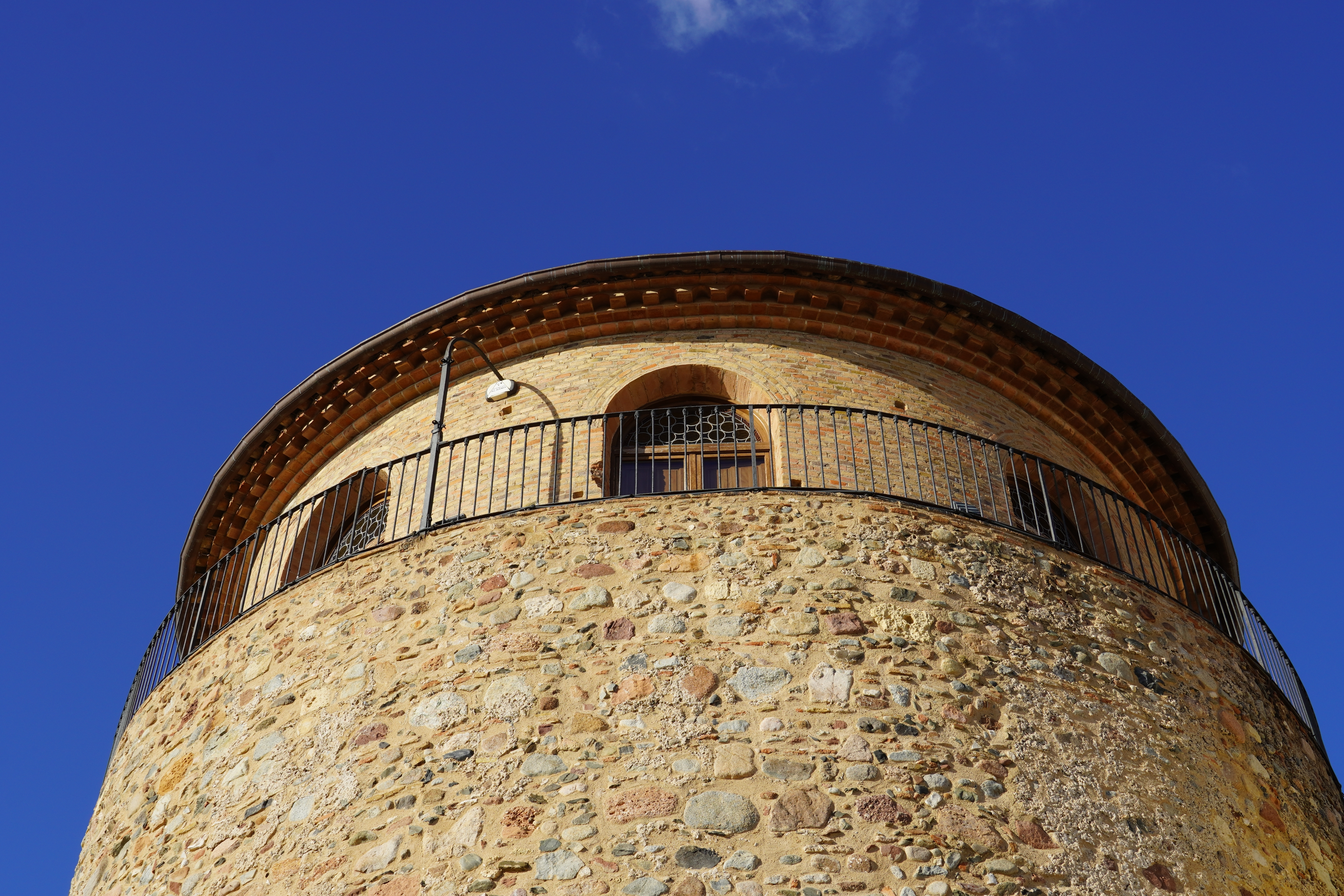 Middelalderligt vagttårn med cirkulær balkon og historisk stenmur mod blå himmel