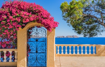Idyllisk udsigt over Middelhavet fra Mallorcas kyst med azurblåt vand, farverige bougainvillea blomster og charmerende spansk villa