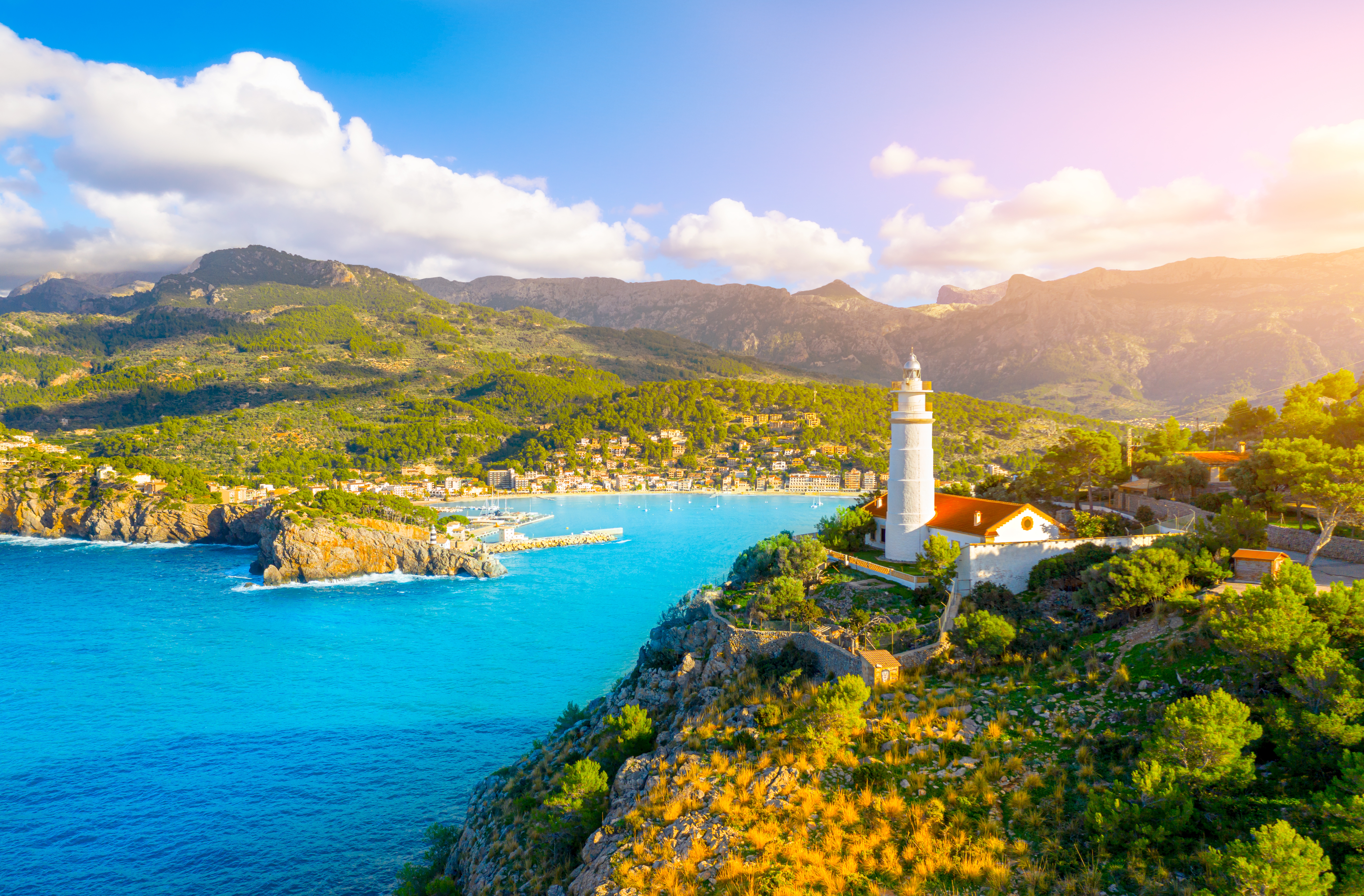 Smukt middelhavs fyrtaarn ved turkis bugt med bjerge og traditionel landsby