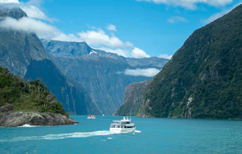 Krydstogtsbaad sejler gennem Milford Sound fjord med dramatiske bjerge og turkisblaat vand i New Zealand