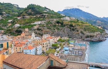 Idyllisk udsigt over Minori på Amalfikysten i Italien med azurblåt Middelhav, grønne pinjetræer og historisk kirke i solskinsvejr