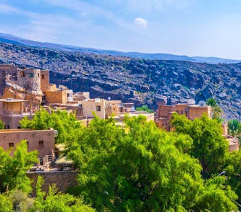 Luftfoto af den traditionelle bjerglandsby Misfat Al Abriyeen i Oman med palmetræer og historiske stenhuse omgivet af grønne terrasseområder