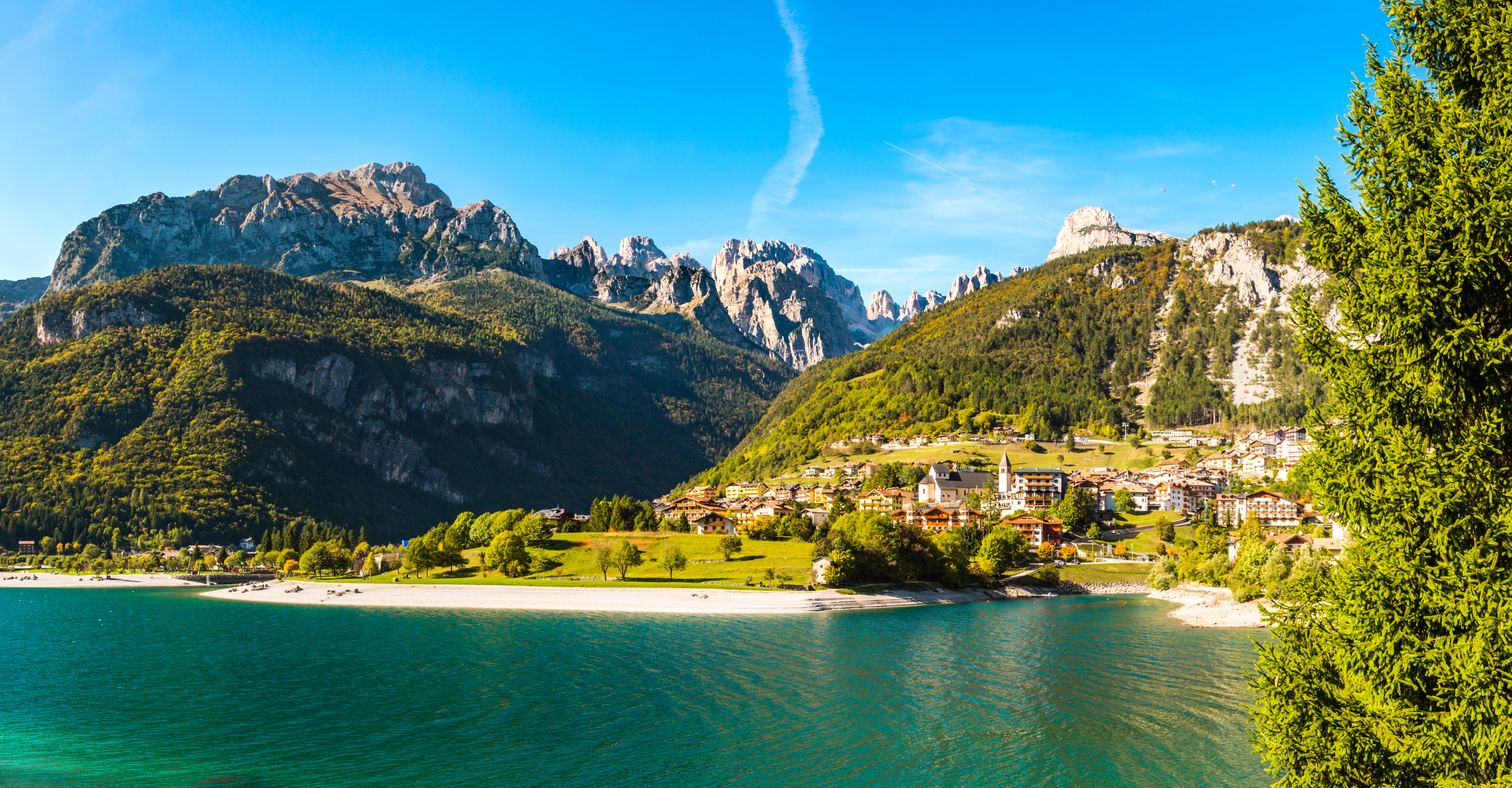 Panoramaudsigt over den charmerende bjergby Molveno ved bredden af den turkisblå Molveno-sø med de dramatiske Brenta Dolomitter i baggrunden, Trentino, Italien