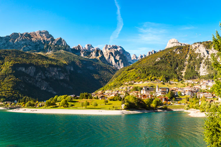 Panoramaudsigt over den charmerende bjergby Molveno ved bredden af den turkisblå Molveno-sø med de dramatiske Brenta Dolomitter i baggrunden, Trentino, Italien