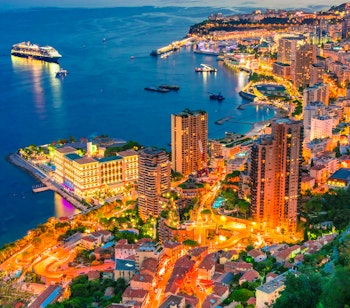 Betagende udsigt over Monaco på den franske riviera ved solnedgang med luksusyachter i havnen og oplyste skyskrabere langs Middelhavets kyst