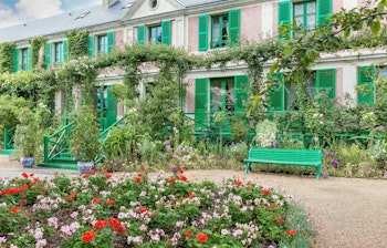 Claude Monets smukke hus i Giverny med grønne skodder og farverig blomsterhave omgivet af klatreroser