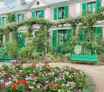 Claude Monets smukke hus i Giverny med grønne skodder og farverig blomsterhave omgivet af klatreroser