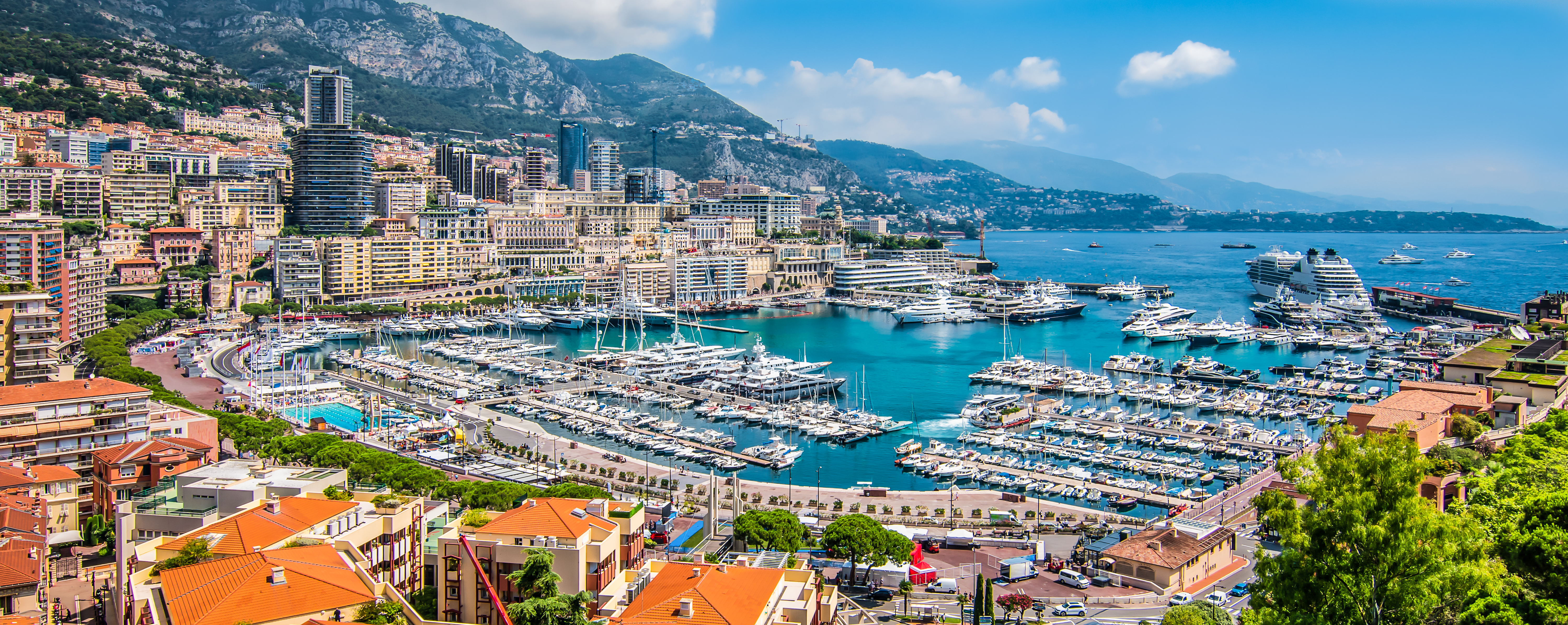Panoramaudsigt over Monte Carlo havn i Monaco med luksusjachter, krydstogtskib og farverig byudsigt mod Middelhavets bjerge