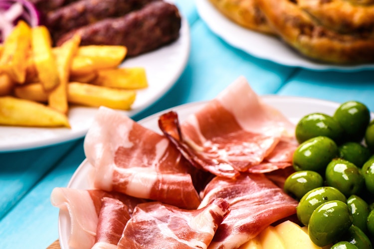 Traditionel montenegrinsk madbræt med Njegusi-skinke, hjemmelavet ost, cevapi, burek, oliven og stegte rejer på rustikt træbord