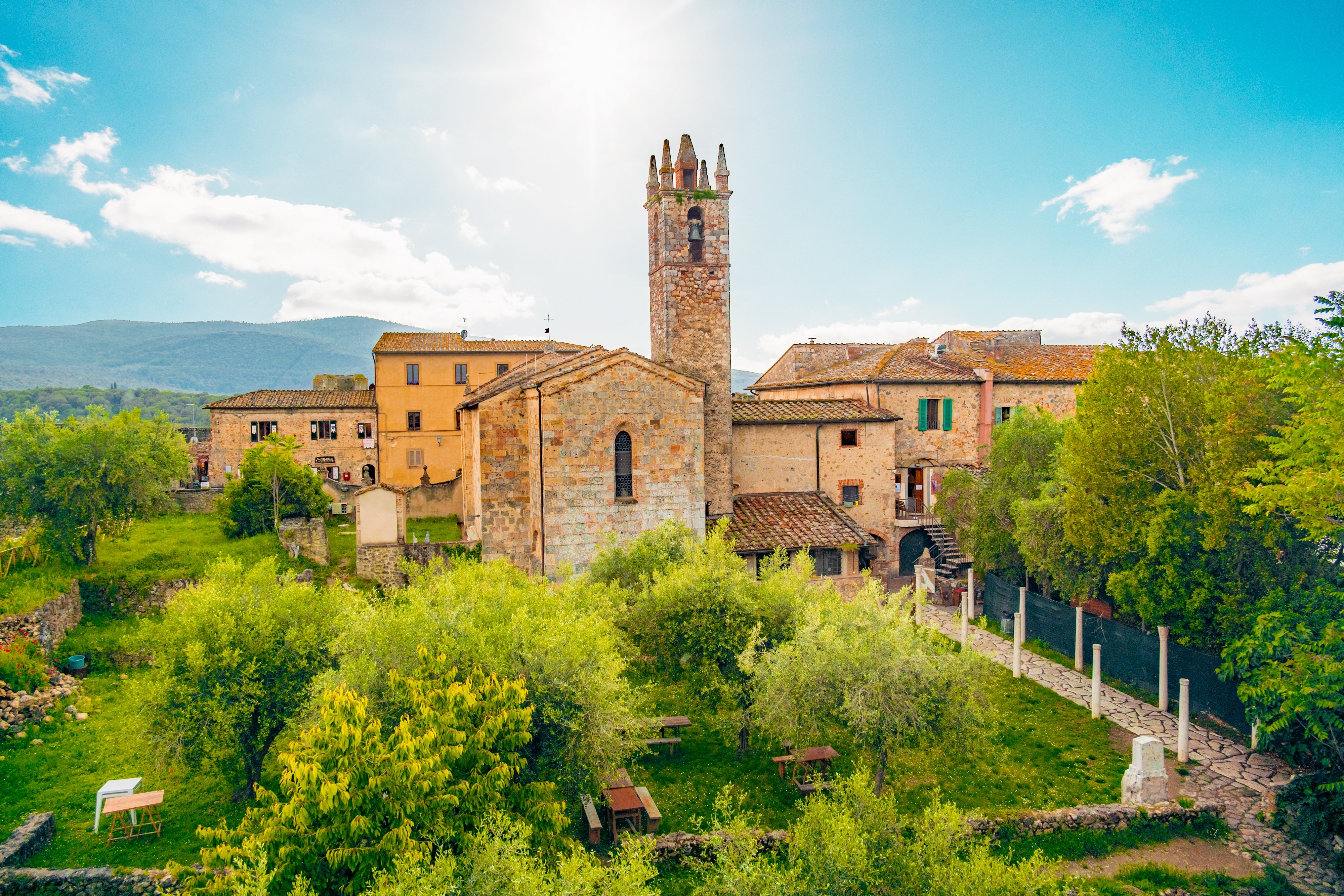 Panoramaudsigt over den middelalderlige bjerglandsby Monteriggioni i Toscana, Italien, med en stentårnskirke omgivet af grønne træer og terrakottafarvet bebyggelse