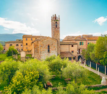 Panoramaudsigt over den middelalderlige bjerglandsby Monteriggioni i Toscana, Italien, med en stentårnskirke omgivet af grønne træer og terrakottafarvet bebyggelse