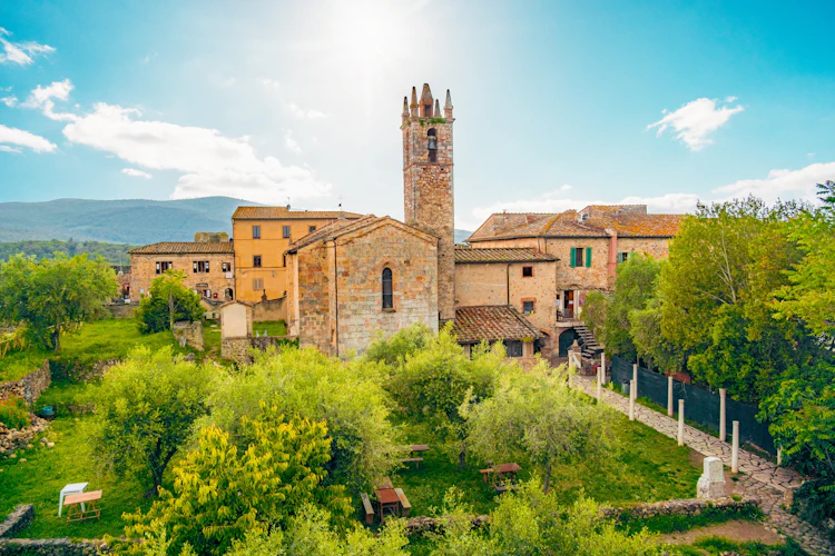 Panoramaudsigt over den middelalderlige bjerglandsby Monteriggioni i Toscana, Italien, med en stentårnskirke omgivet af grønne træer og terrakottafarvet bebyggelse