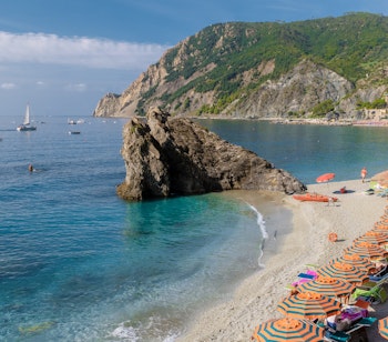 Farverige strandparasoller og liggestole på Spiaggia di Fegina stranden i Monterosso al Mare, Cinque Terre. Idyllisk italiensk kystferie med turkisblåt Middelhav på en solrig sommerdag.