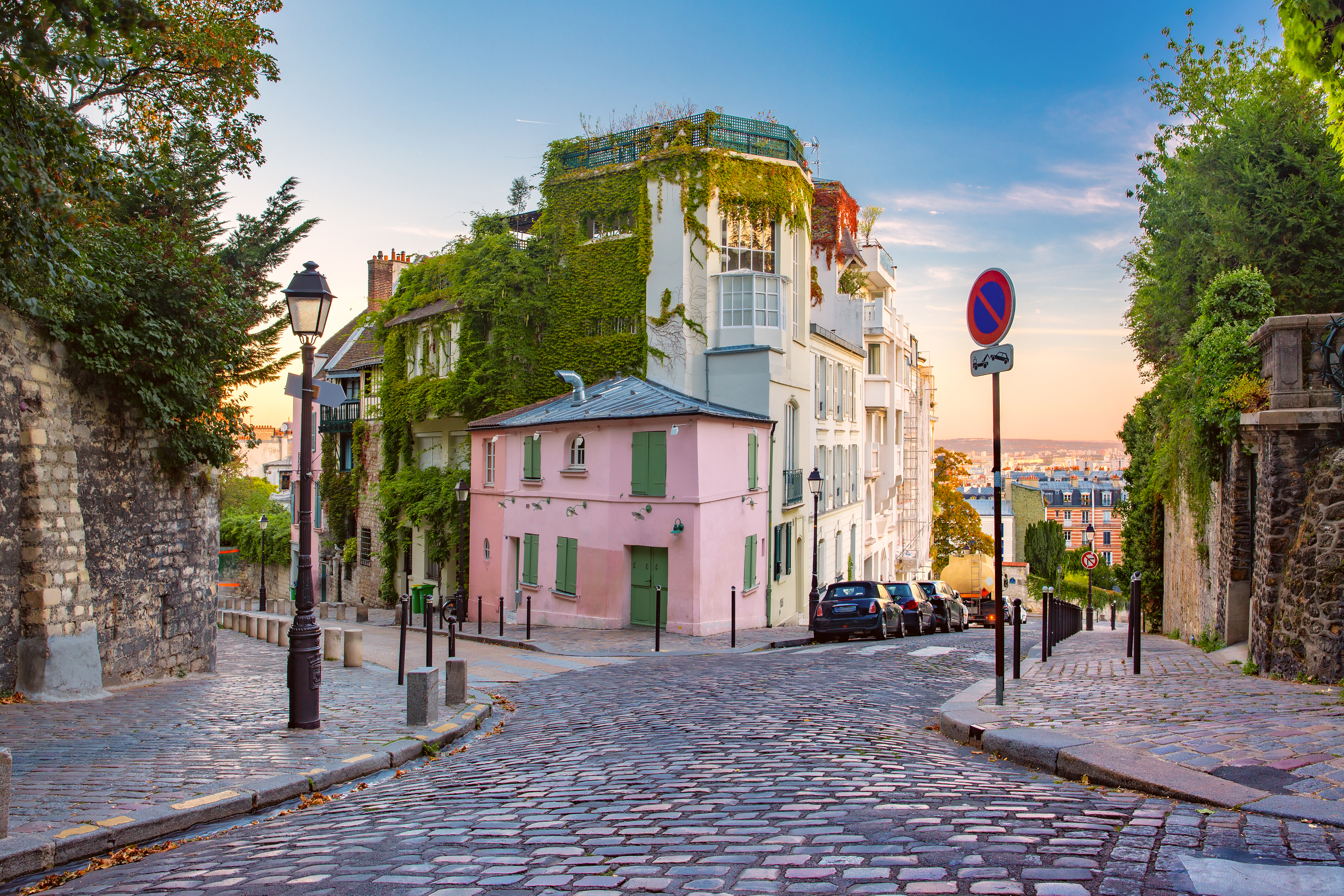 Charmerende brolagt gade i Montmartre, Paris, med et lyserødt hus dækket af grøn vedbend i det varme solopgangslys