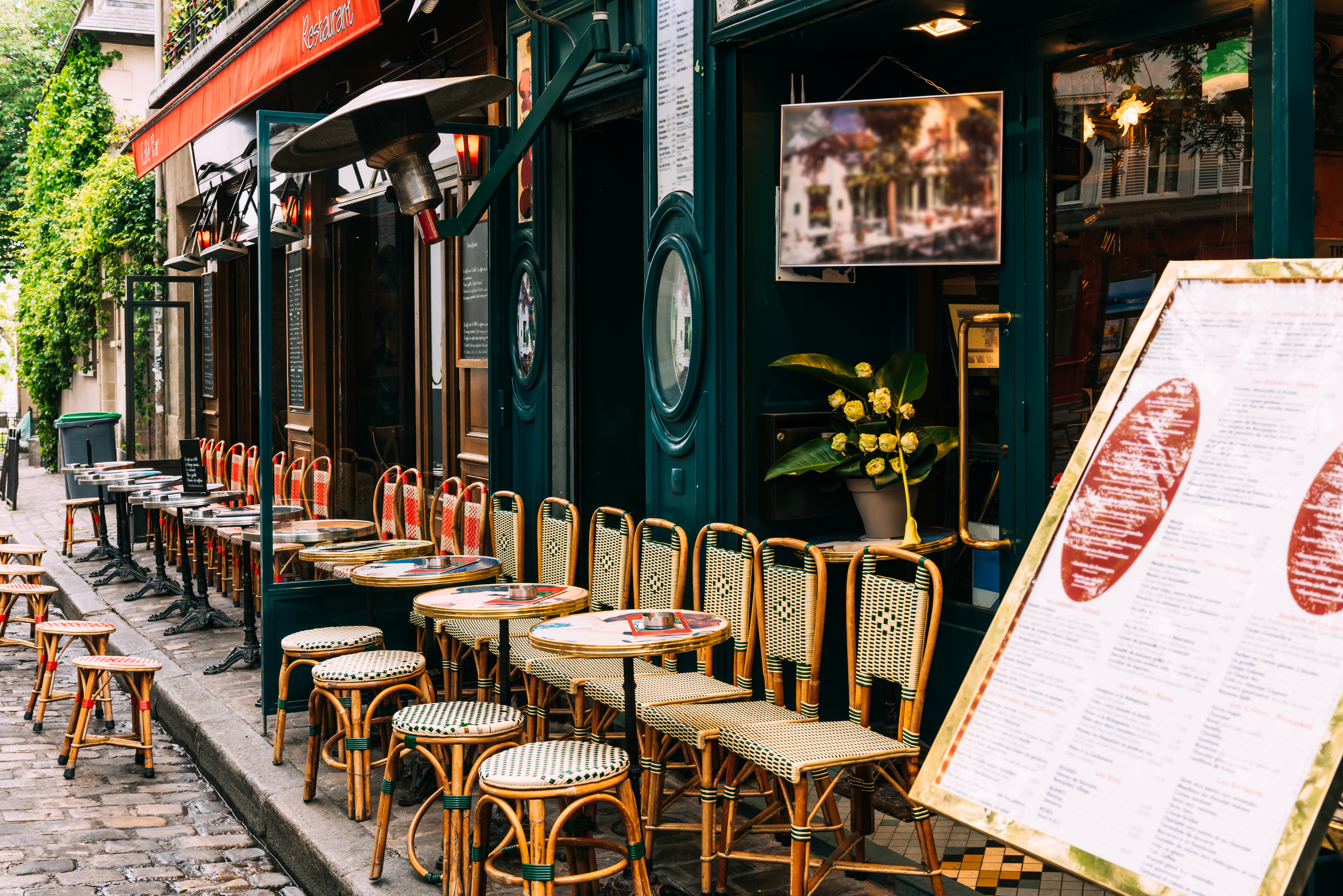 Hyggelig cafe-terrasse med flettede stole og runde borde på brolagte gader i Montmartre, Paris