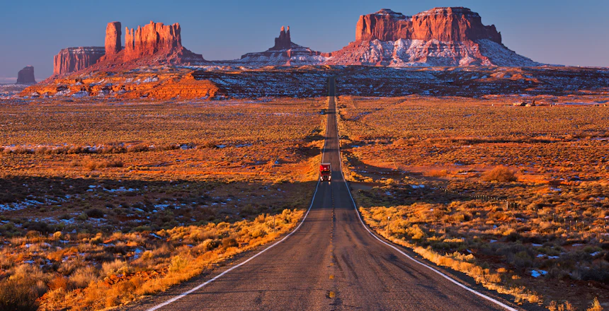 Dramatisk ørkenvej til Monument Valley med røde klipper ved solnedgang