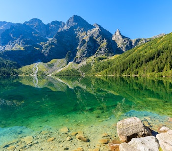Betagende udsigt over den smaragdgrønne Morskie Oko sø omgivet af de majestætiske Tatra-bjerge i Polen med klart vand der reflekterer fyrretræer og bjergtoppe