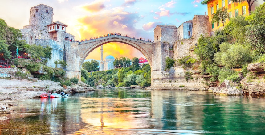 Betagende udsigt over Mostars historiske bro ved solnedgang med traditionelle huse og minareter langs Neretva-floden i Bosnien-Hercegovina