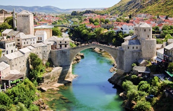 Panoramaudsigt over den historiske by Mostar med den ikoniske Stari Most bro, der spaender over den smaragdgroenne Neretva-flod, omgivet af traditionelle stenbygninger og moskeer i Bosnien-Hercegovina