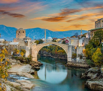 Den historiske Stari Most bro over Neretva-floden i Mostar ved solnedgang med traditionel ottomansk arkitektur og bjerge i baggrunden