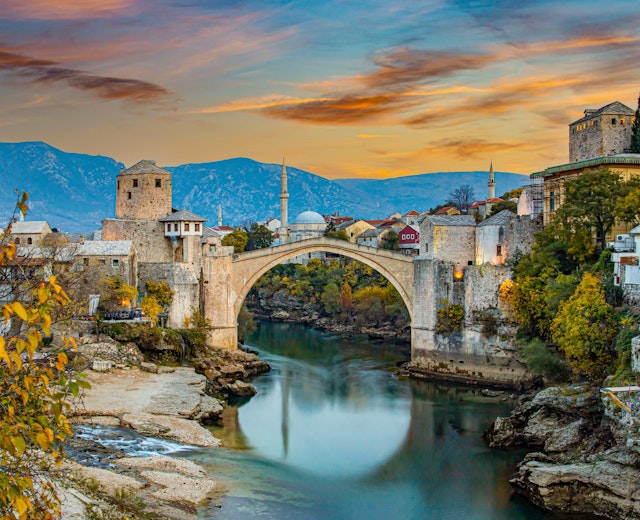 Den historiske Stari Most bro over Neretva-floden i Mostar ved solnedgang med traditionel ottomansk arkitektur og bjerge i baggrunden
