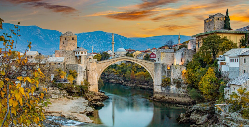 Den historiske Stari Most bro over Neretva-floden i Mostar ved solnedgang med traditionel ottomansk arkitektur og bjerge i baggrunden