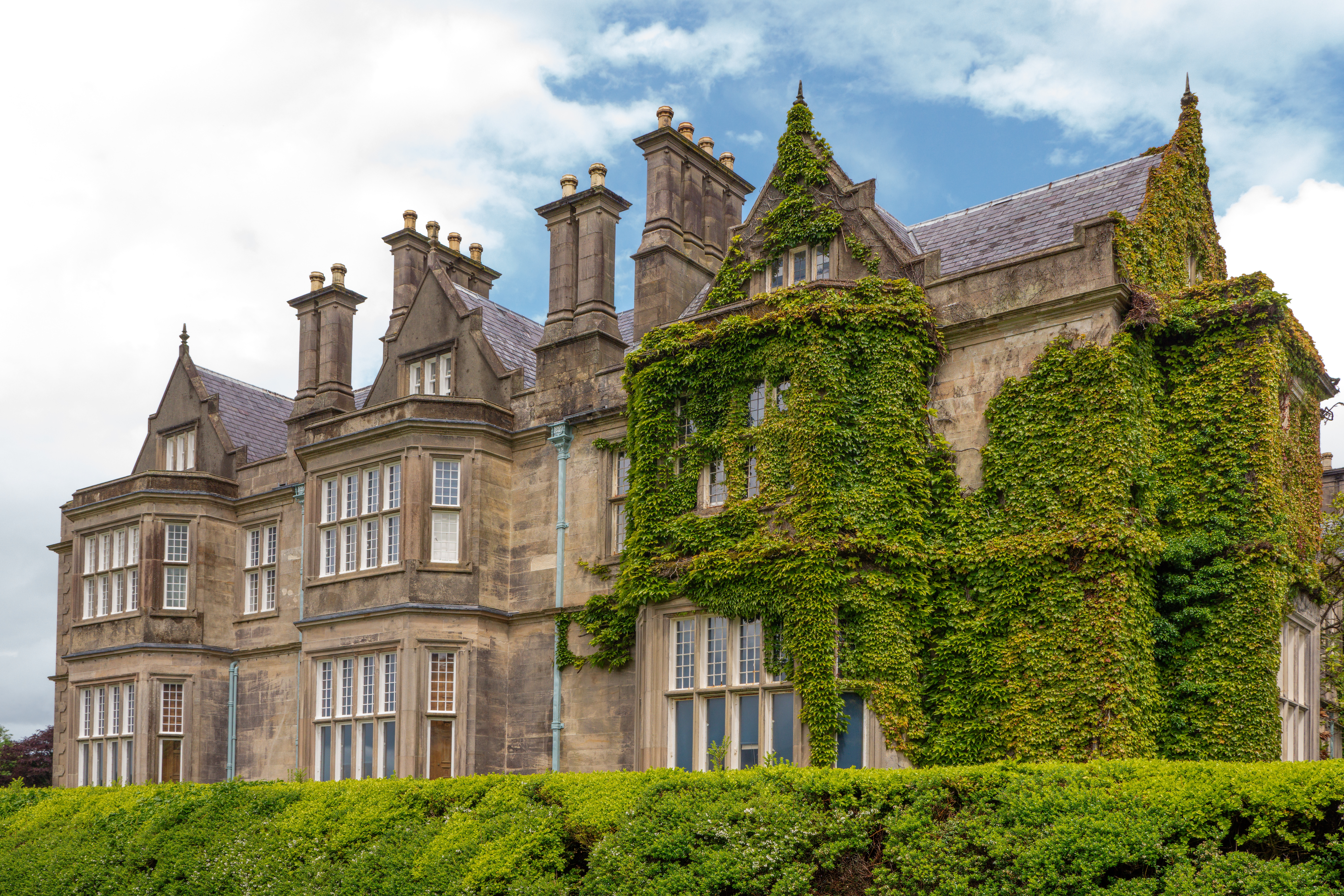 Muckross House i Killarney National Park, Irland – en smuk victoriansk herregård dækket af vedbend med velklippede hække i forgrunden