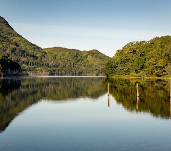 Fredelig udsigt over Muckross-søen i Killarney Nationalpark med bjergenes og himlens spejling i det stille vand, en naturperle i County Kerry, Irland
