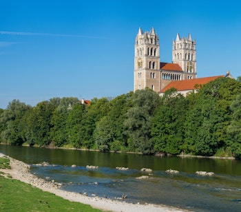 Smuk panoramaudsigt over Isar-floden i München med de to tårne fra St. Maximilian kirken, omgivet af frodige grønne parker og træer under en klar blå sommerhimmel