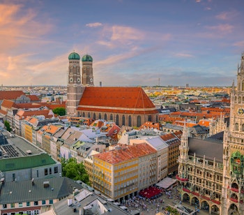 Panoramaudsigt over Münchens historiske bycentrum ved solnedgang med Marienplatz rådhus og Frauenkirches karakteristiske tårne