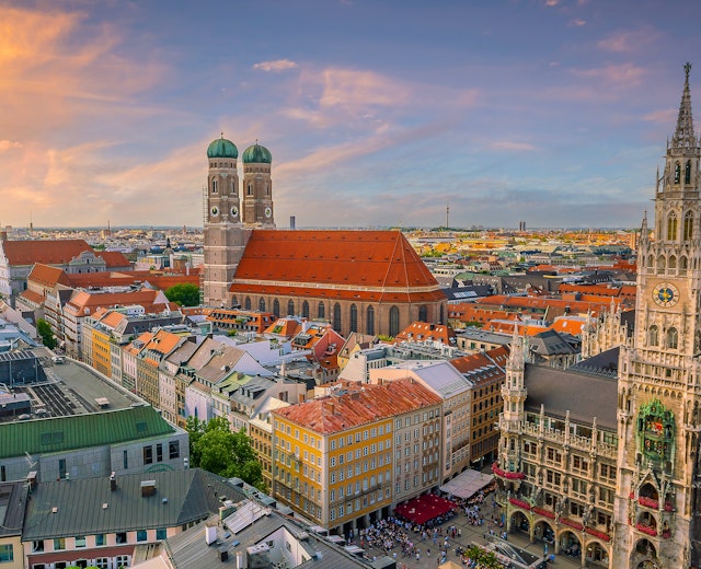 Panoramaudsigt over Münchens historiske bycentrum ved solnedgang med Marienplatz rådhus og Frauenkirches karakteristiske tårne