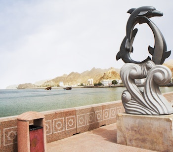 Muscat Corniche i Oman med elegante delfin-statuer langs den velholdte strandpromenade med udsigt over havet og bjergene