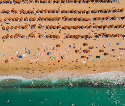 Luftfoto af den berømte Lia-strand på Mykonos med krystalklart turkisblåt vand, hvidt sand og organiserede rækker af solsenge og parasoller