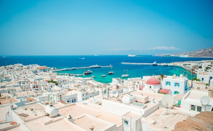 Panoramaudsigt over traditionel græsk landsby på Mykonos med hvidkalkede huse, blå detaljer og lille havn med både langs den ægæiske kyst