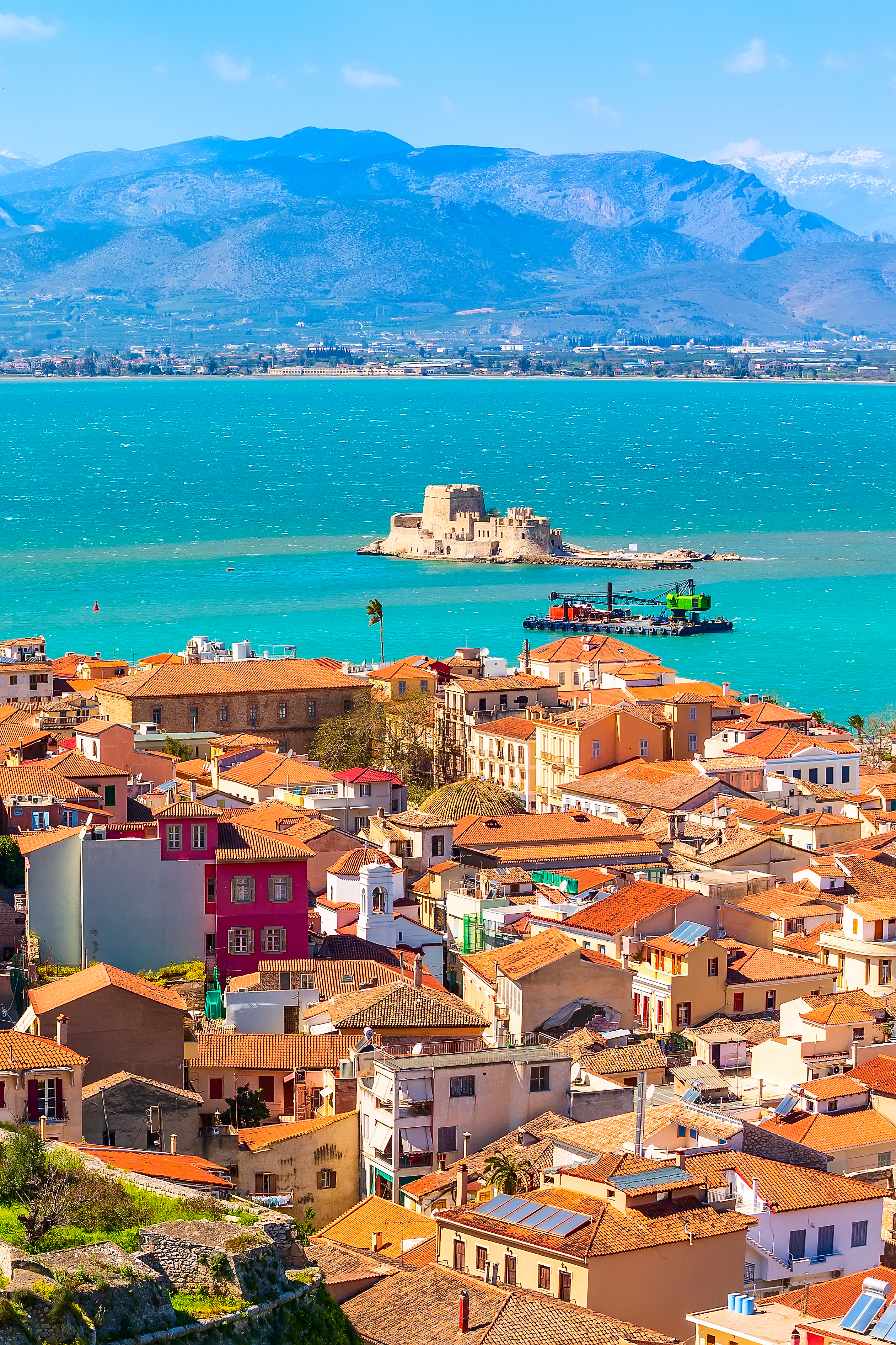 Betagende luftpanorama over Nafplio, Grækenlands første hovedstad, med den gamle bydels terrakottafarvede tage, venetiansk arkitektur og den ikoniske Bourtzi-fæstning i bugten, omgivet af det blå Middelhav og Peloponnes' bjerge