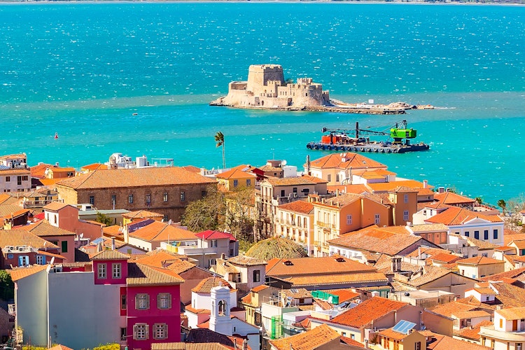 Betagende luftpanorama over Nafplio, Grækenlands første hovedstad, med den gamle bydels terrakottafarvede tage, venetiansk arkitektur og den ikoniske Bourtzi-fæstning i bugten, omgivet af det blå Middelhav og Peloponnes' bjerge