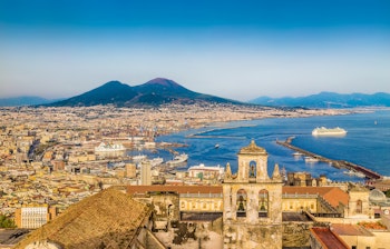 Malerisk panoramaudsigt over Napoli med Vesuv-vulkanen i baggrunden badet i gyldent solnedgangslys ved Middelhavet i Syditalien