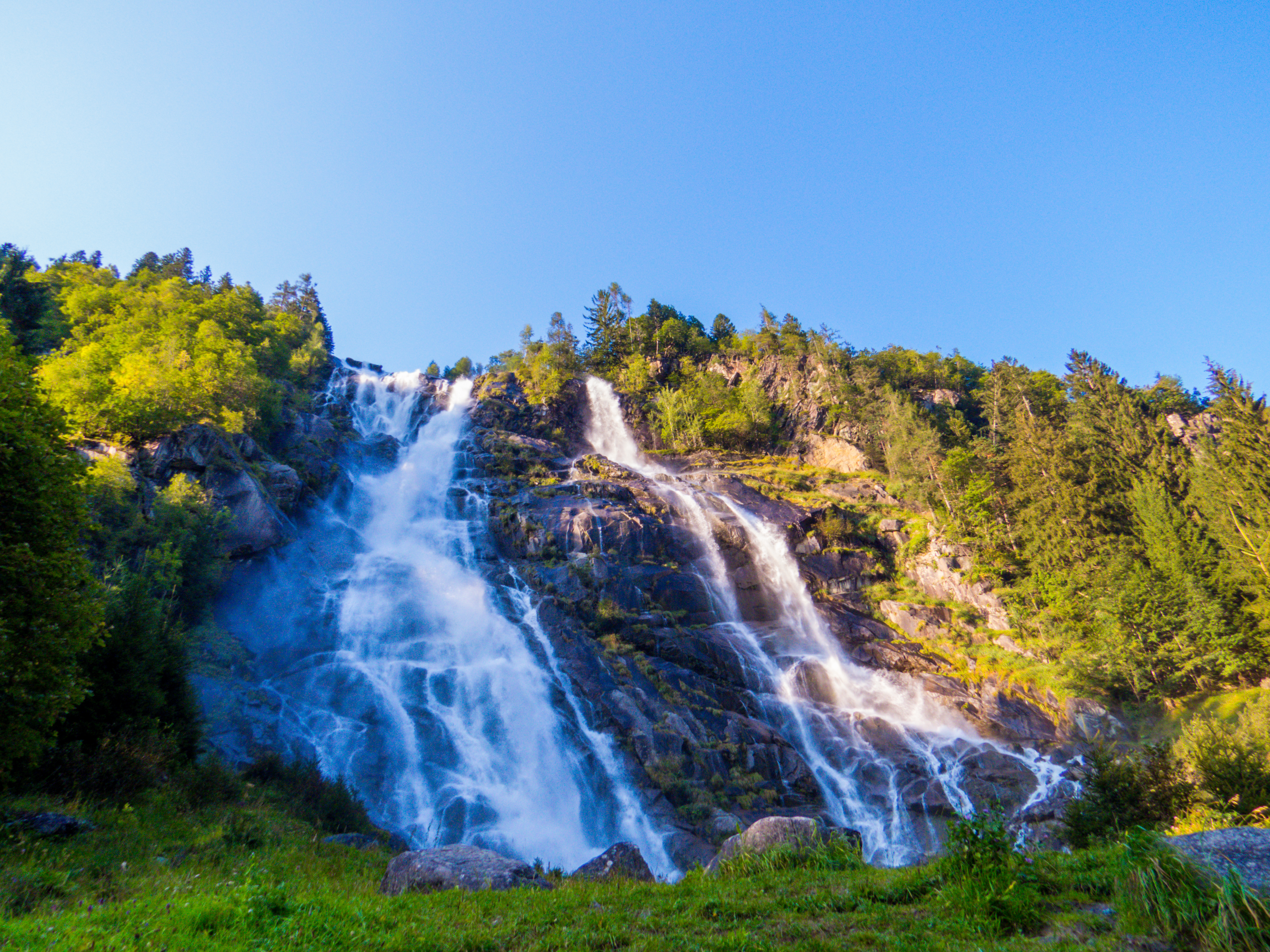 Nardis Laris vandfald styrter ned ad klippefyldte skråninger omgivet af frodig grøn skov i Adamello Brenta Naturpark, Trentino, Italien