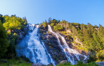 Nardis Laris vandfald styrter ned ad klippefyldte skråninger omgivet af frodig grøn skov i Adamello Brenta Naturpark, Trentino, Italien