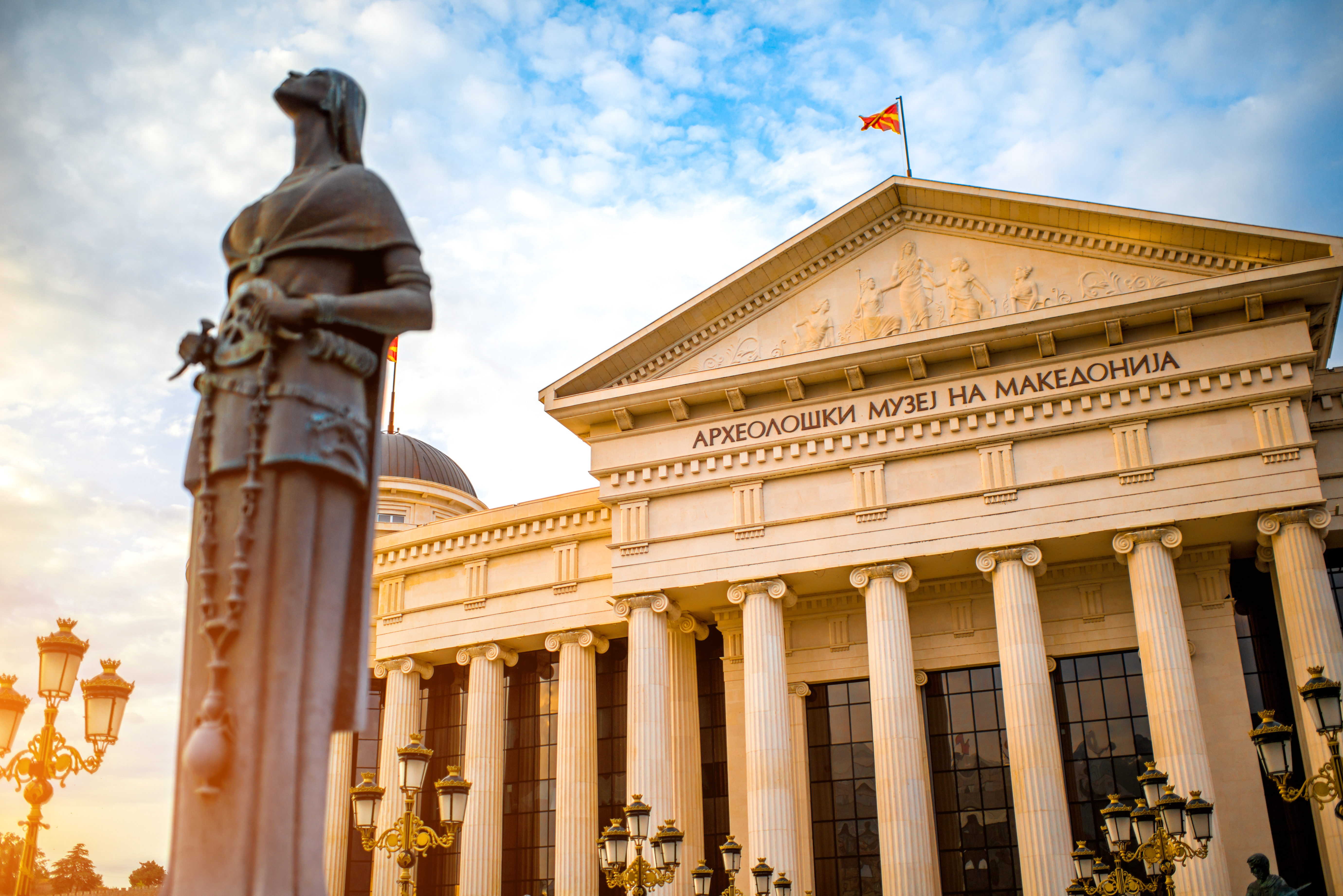 Det historiske nationalmuseum i Skopje med Moder Teresa monumentet i forgrunden under blå himmel