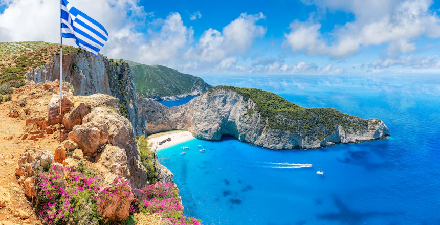 Den berømte Navagio strand med skibsvrag på Zakynthos, Grækenland, med krystalklart turkisblåt vand og det græske flag på klippen