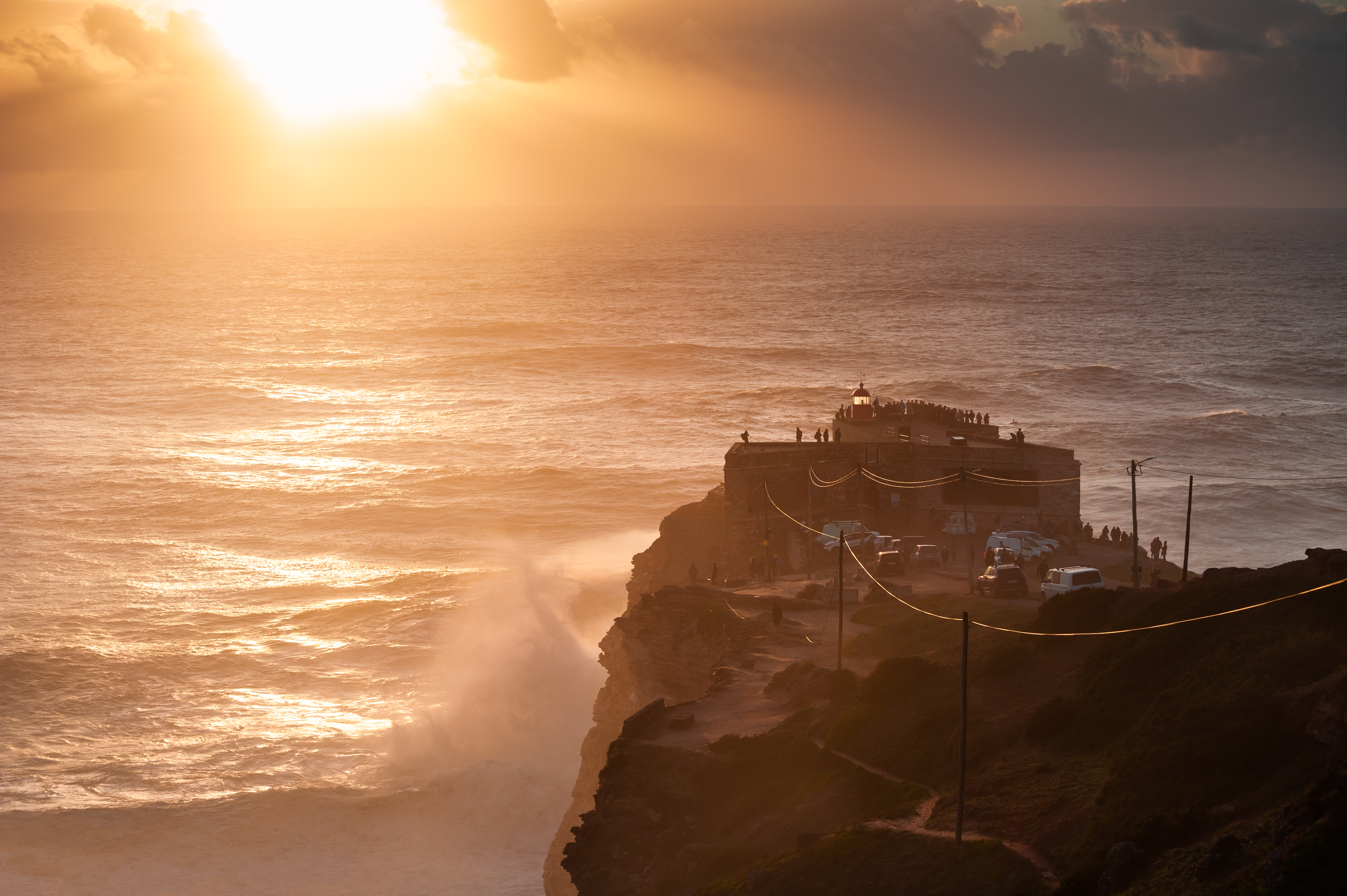 Betagende solnedgang ved fyrtårnet i Nazaré, Portugal, med imponerende bølger fra Atlanterhavet der slår mod kysten
