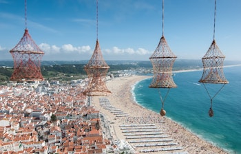 Betagende udsigt over Nazaré i Portugal fra Sítio-udsigtspunktet med traditionelle fiskenet i forgrunden og den lange sandstrand langs Atlanterhavet