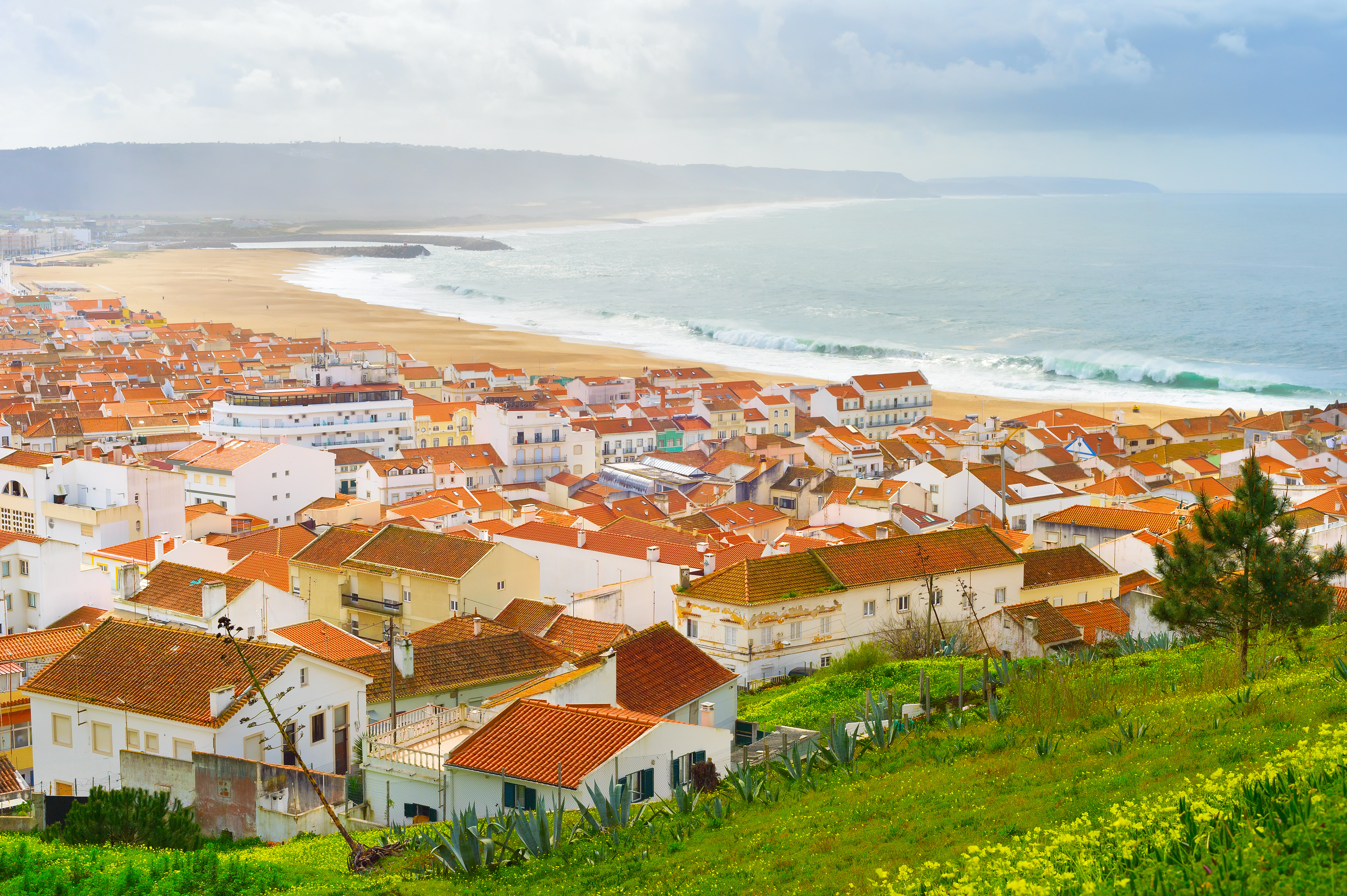 Luftfoto af Nazare i Portugal med farverige tage og Atlanterhavet strand